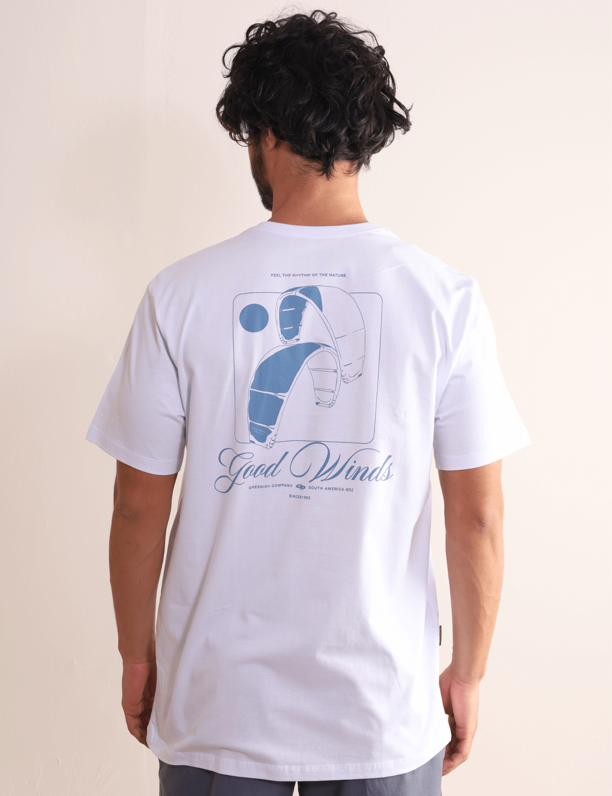 Homem vestindo camiseta Greenish Kites & Good Winds branca com arte de kite nas costas.