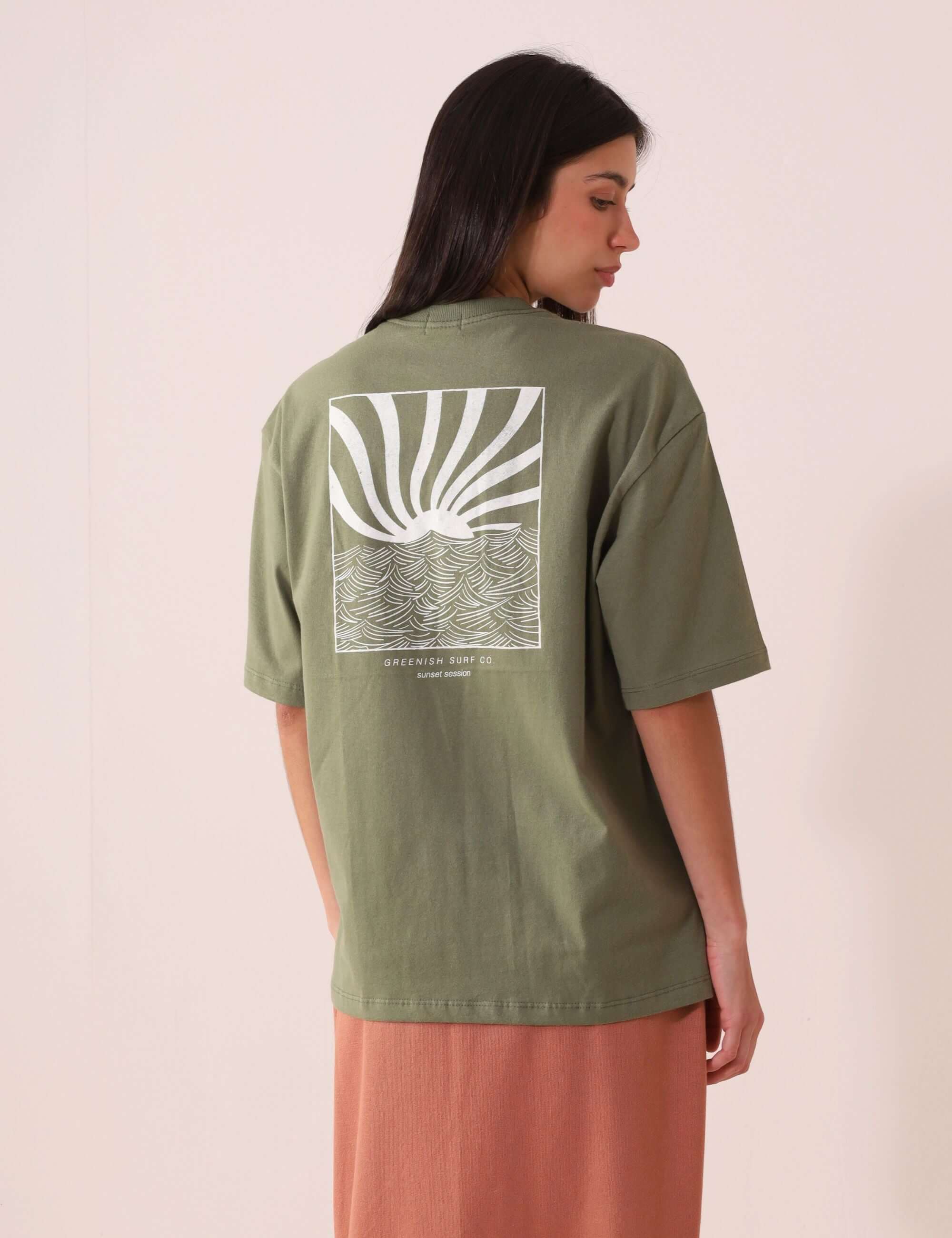 Modelo usando CAMISETA OVERSIZED SUNSET SESSION - VERDE da Greenish com estampa de ondas e pôr do sol nas costas, estilo e conforto.