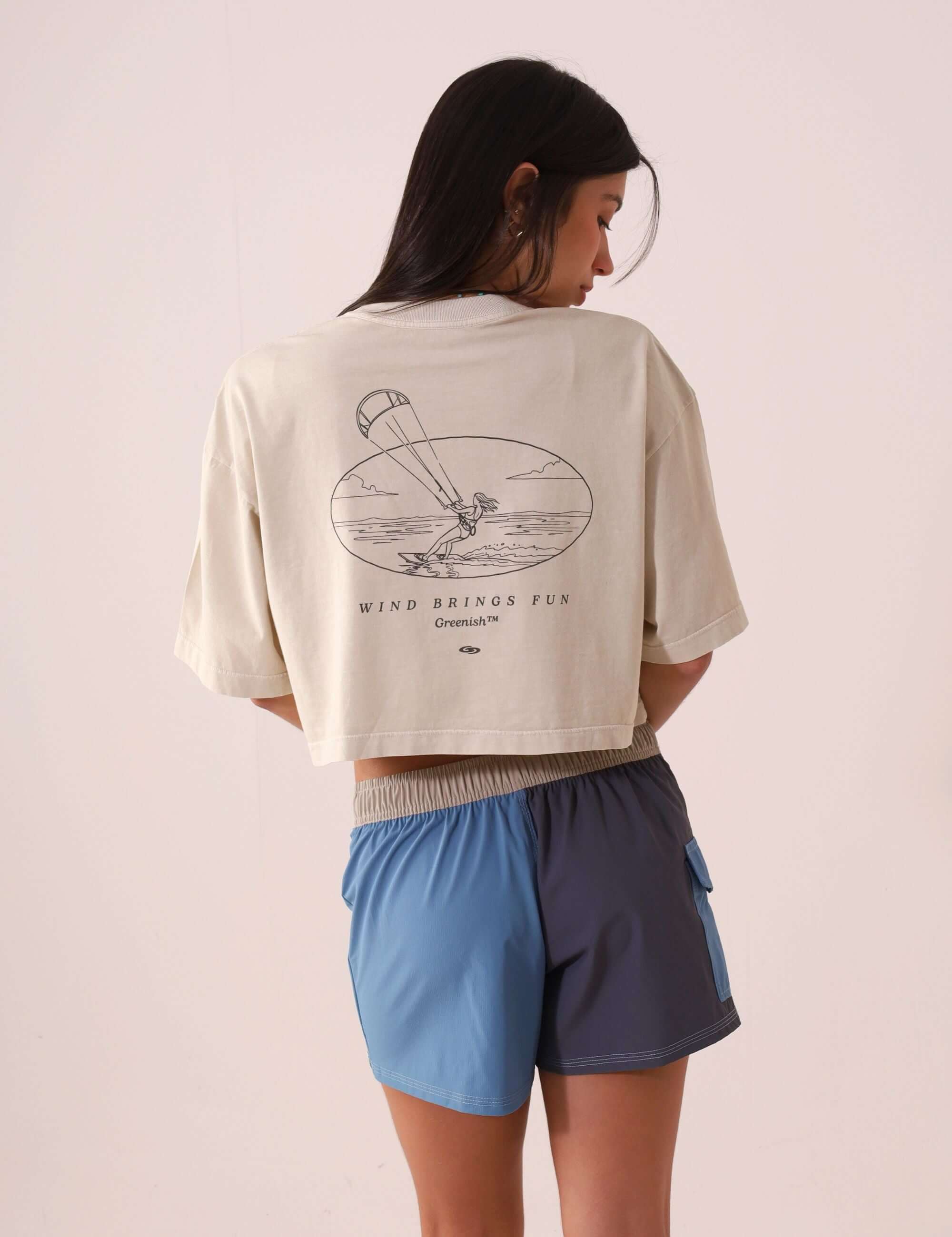 Mulher vestindo SHORT SPORT TALITA - AZUL da marca Greenish, visto de costas com camiseta curta e estampa de vento e diversão.