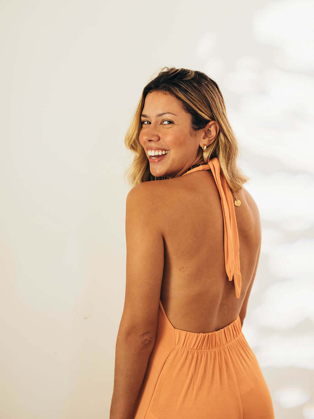 Mulher sorrindo com macacão laranja Greenish, decote em V e costas nuas, exalando estilo e elegância.