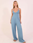 Modelo vestindo Macacão canelado Mariela - Azul Indigo com decote V e alças ajustáveis, destacando conforto e elegância.