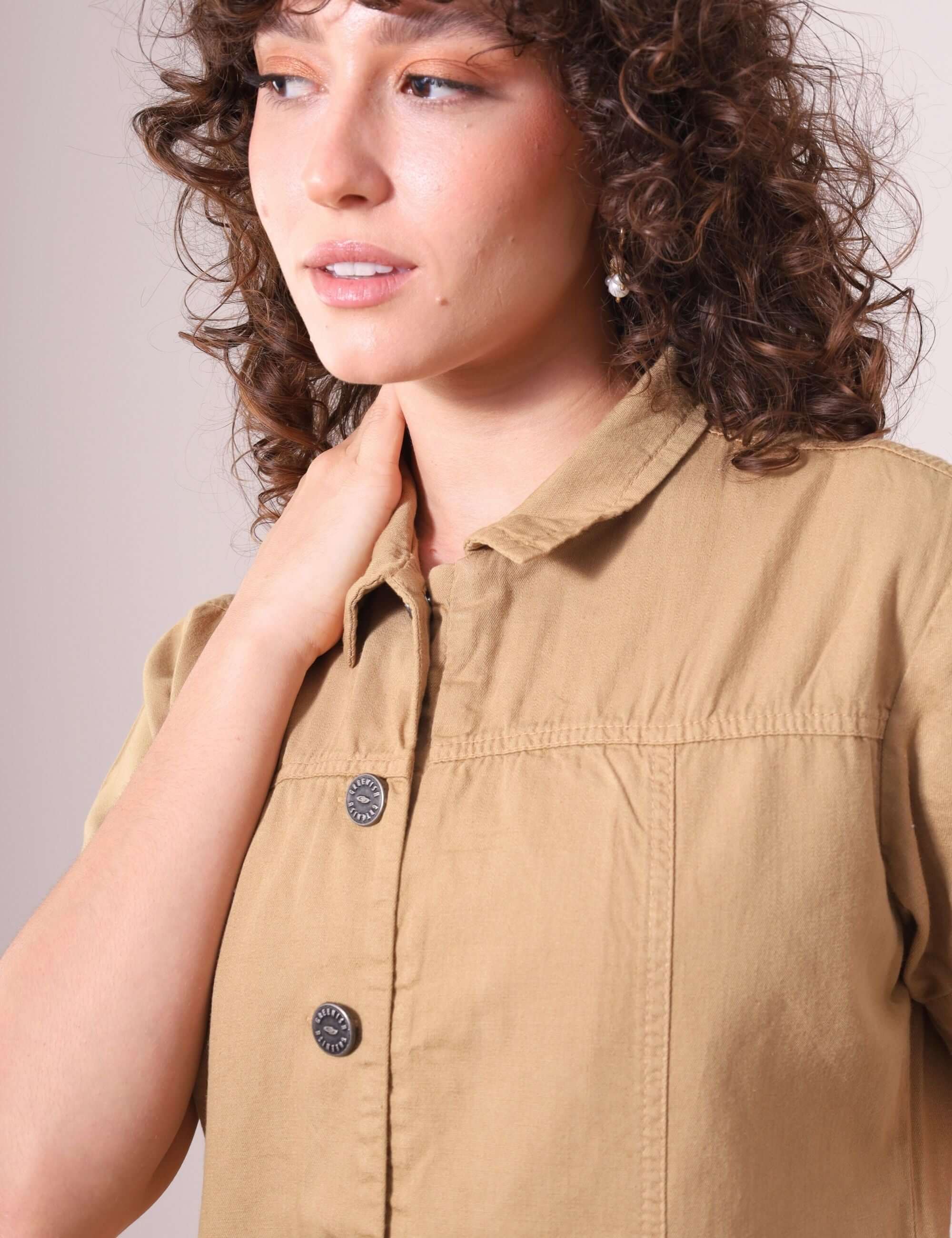 Mulher vestindo o Macacão Ivy Bege da Greenish, destacando gola estruturada e botões frontais. Estilo utilitário e conforto em sarja 100% algodão.