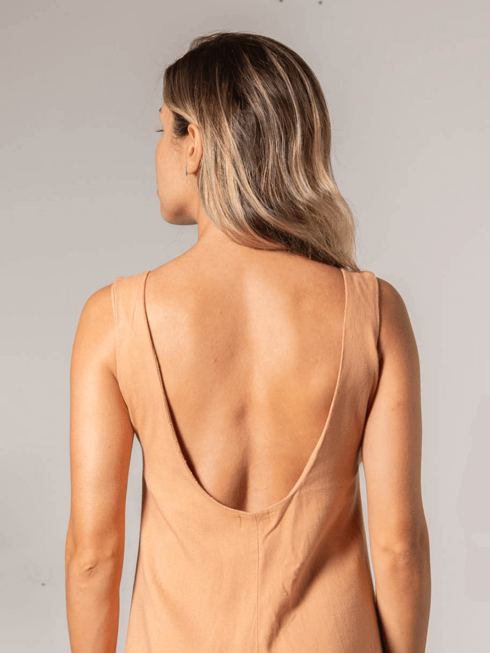 Mulher usando macacão Lauren coral da Greenish, detalhe das costas com decote profundo.