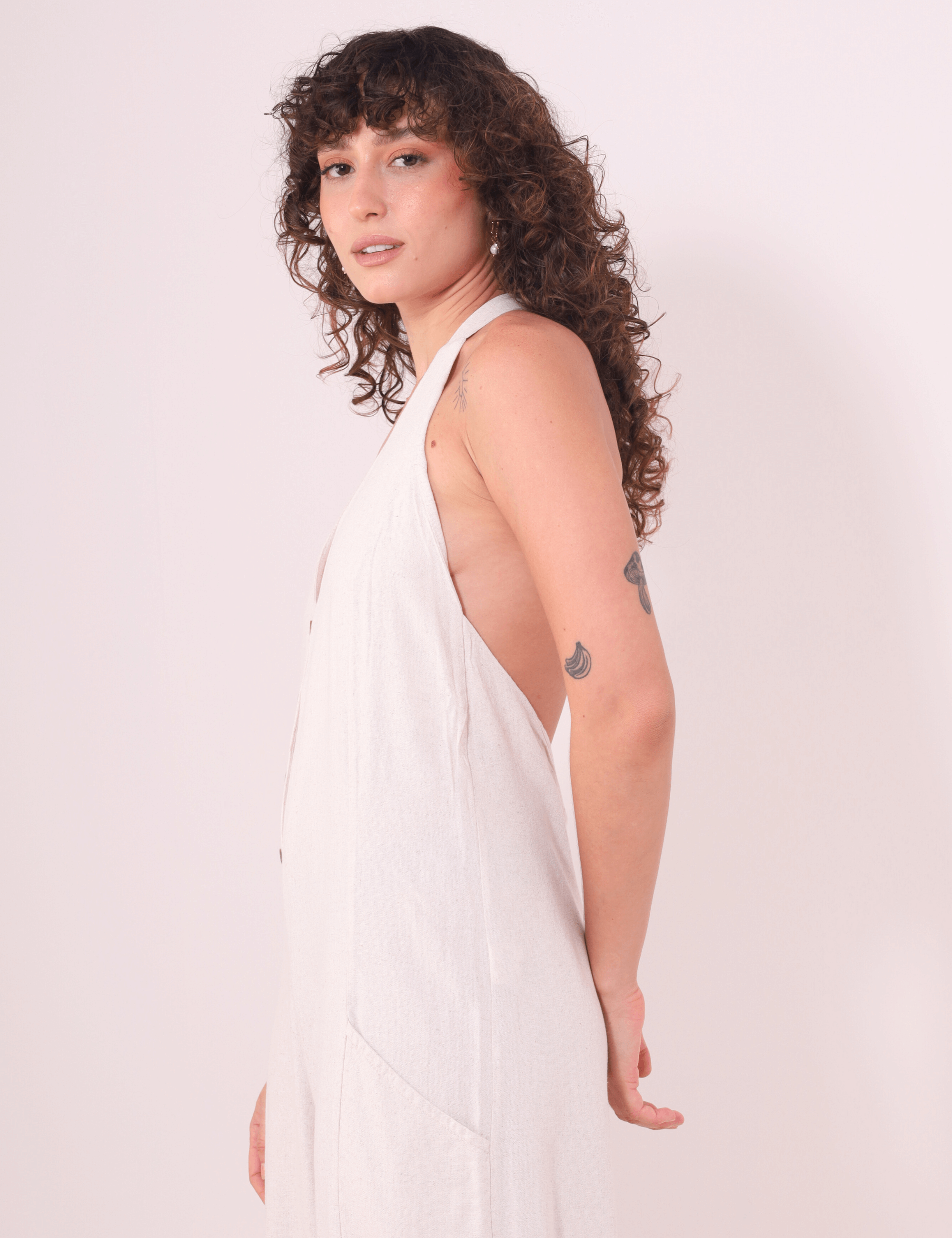 Modelo vestindo Macacão Longo Gaia - Natural da Greenish, em linho washed com decote halter e bolsos, destacando fluidez e leveza.