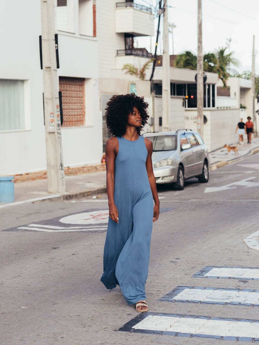 Mulher usando macacão midi Yala azul da marca Greenish, caminhando na rua, estilo moderno e confortável.