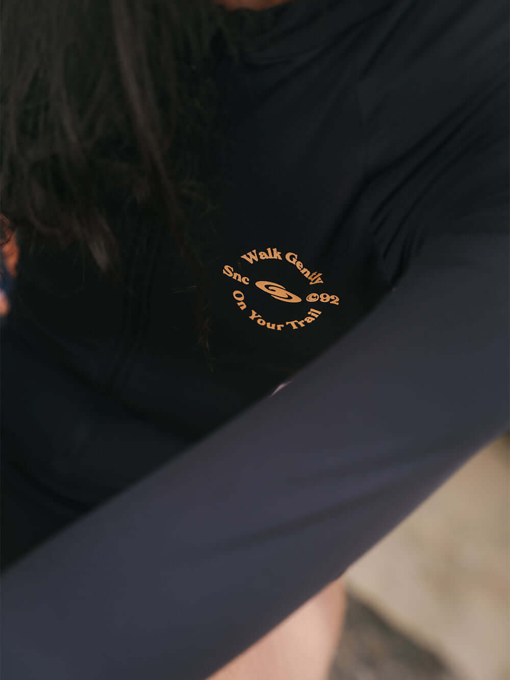 Close-up of a black long-sleeve fabric with an orange logo, featuring the phrase 'Walk Gently' and a playful design.