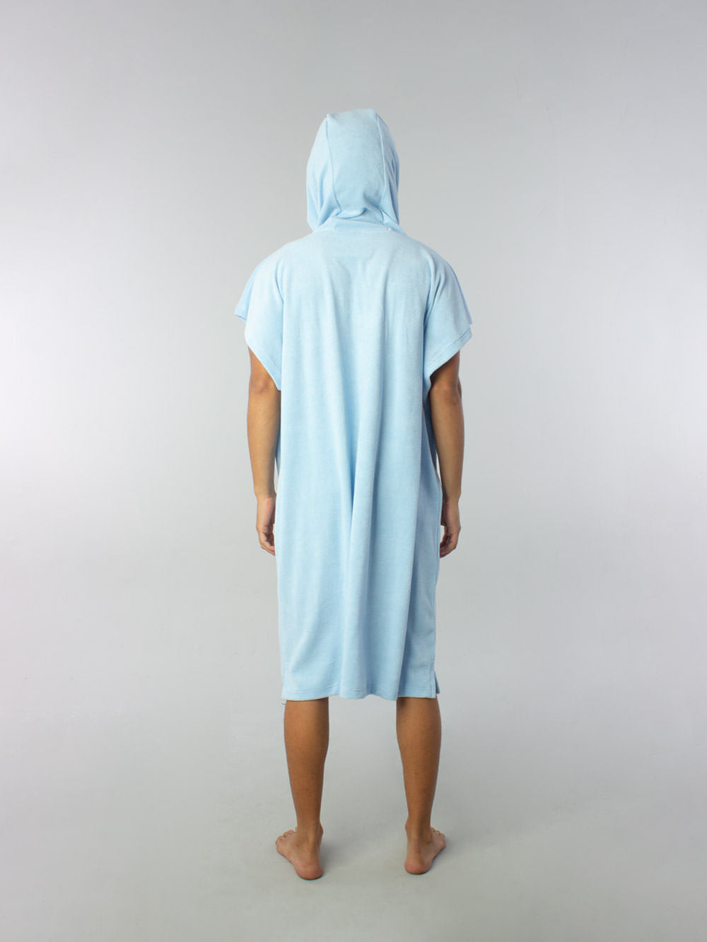 Modelo usando poncho adulto azul claro da Greenish, visto de costas, ideal para praia e esportes aquáticos.