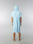 Modelo usando poncho adulto azul claro da Greenish, visto de costas, ideal para praia e esportes aquáticos.