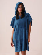 Mulher vestindo PONCHO CURTO CANELADO - AZUL da marca Greenish, ideal para aquecer e trocar na praia, com bolsos frontais e tecido atoalhado.