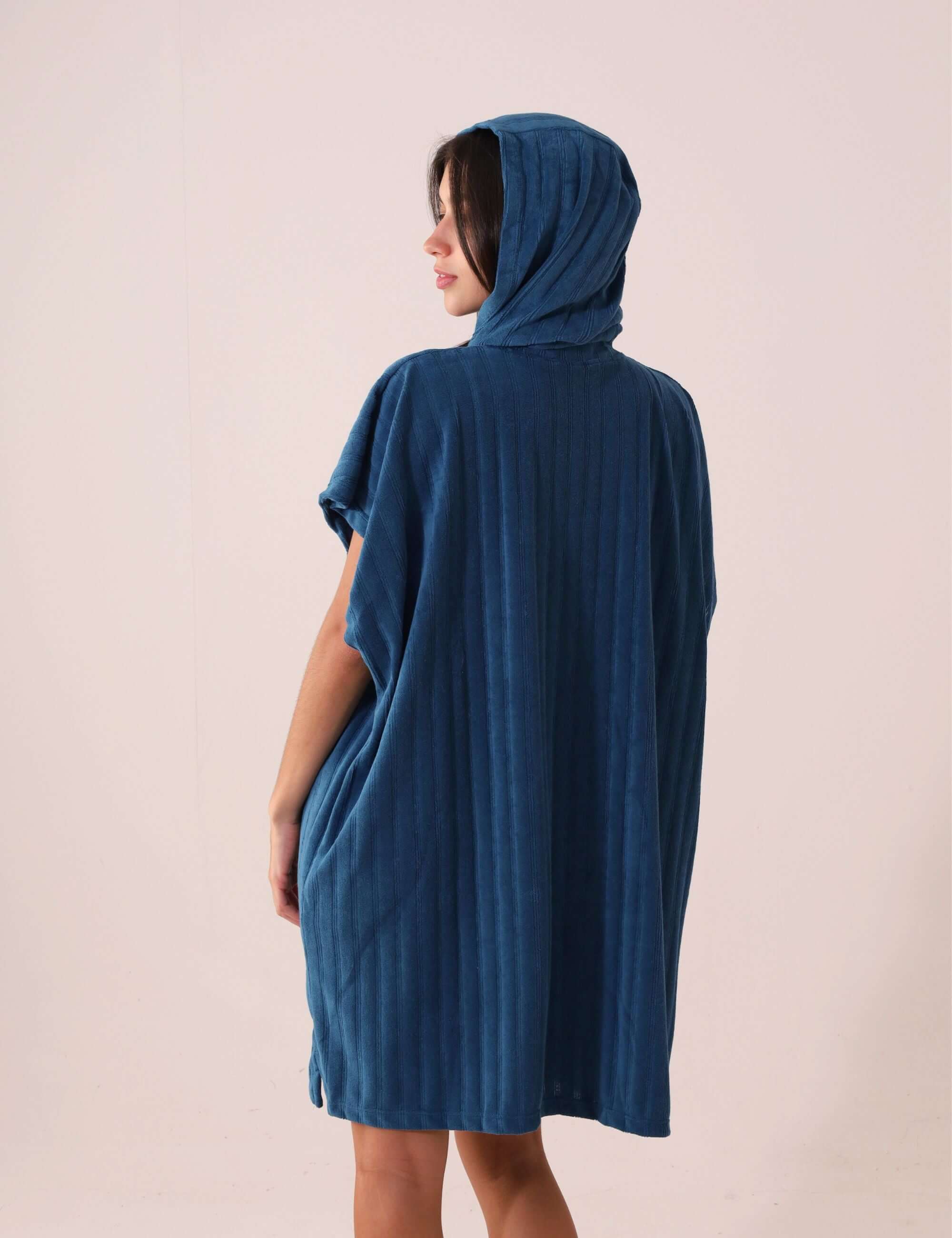 Pessoa vestindo PONCHO CURTO CANELADO - AZUL da Greenish, ideal para aquecer e trocar na praia, tecido atoalhado de secagem rápida.