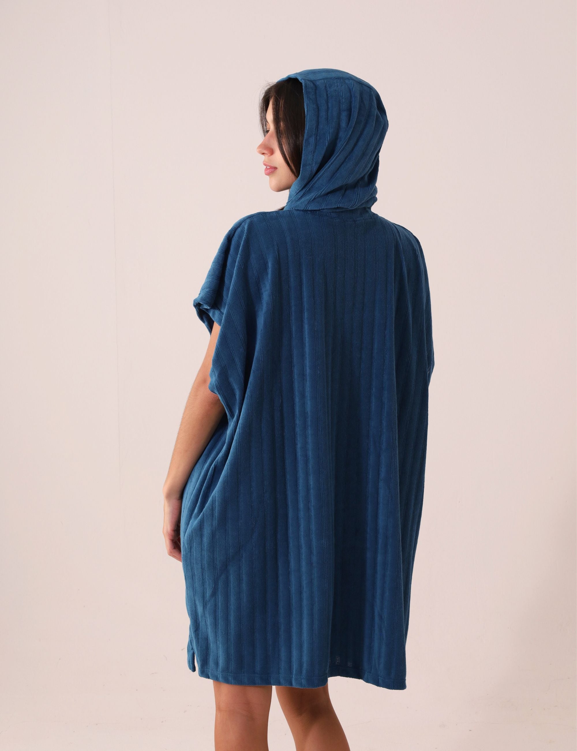 Pessoa vestindo PONCHO CURTO CANELADO - AZUL da Greenish, ideal para aquecer e trocar na praia, tecido atoalhado de secagem rápida.