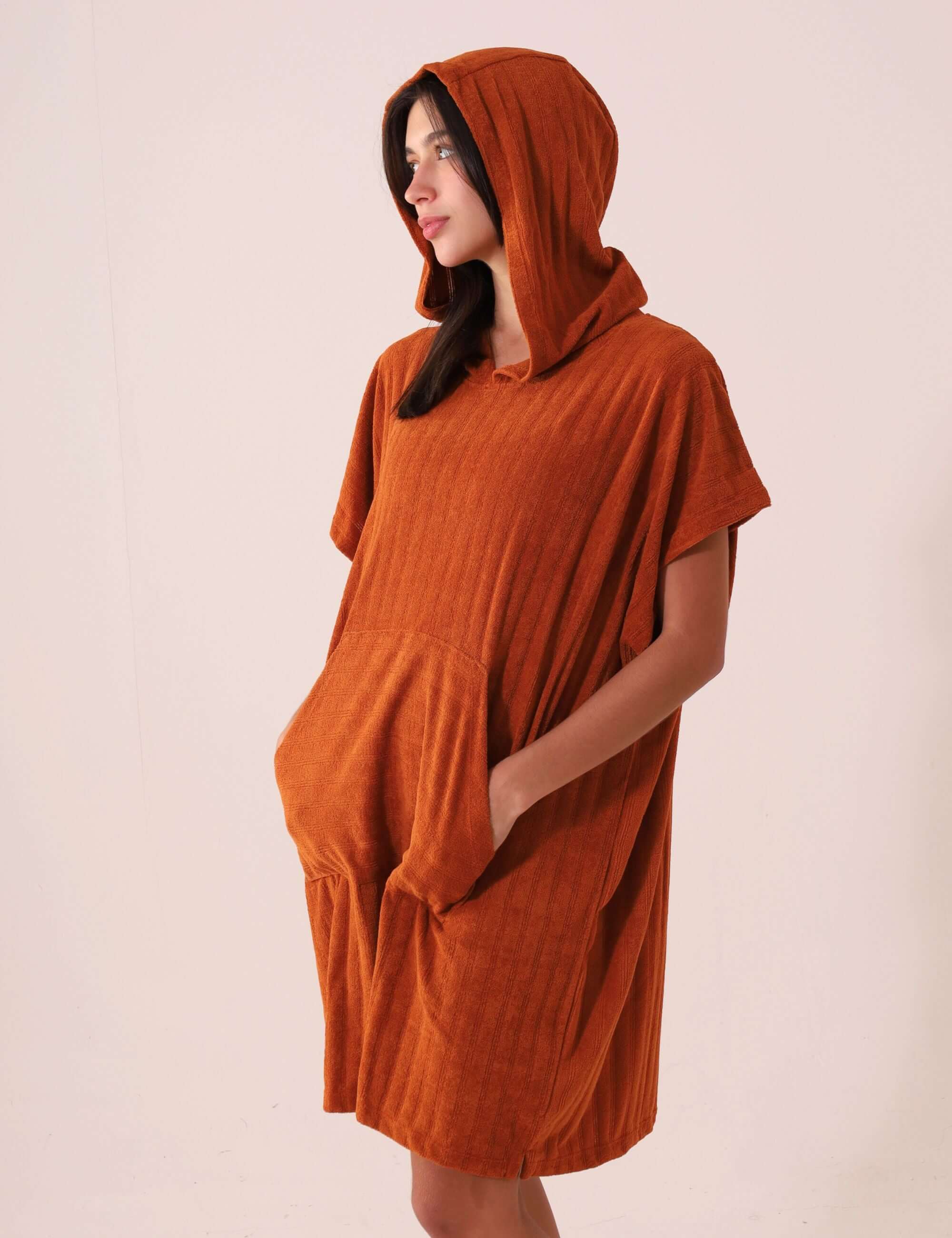 Mulher vestindo PONCHO CURTO CANELADO - CARAMELO da marca Greenish, com bolsos canguru, capuz, tecido atoalhado e secagem rápida.