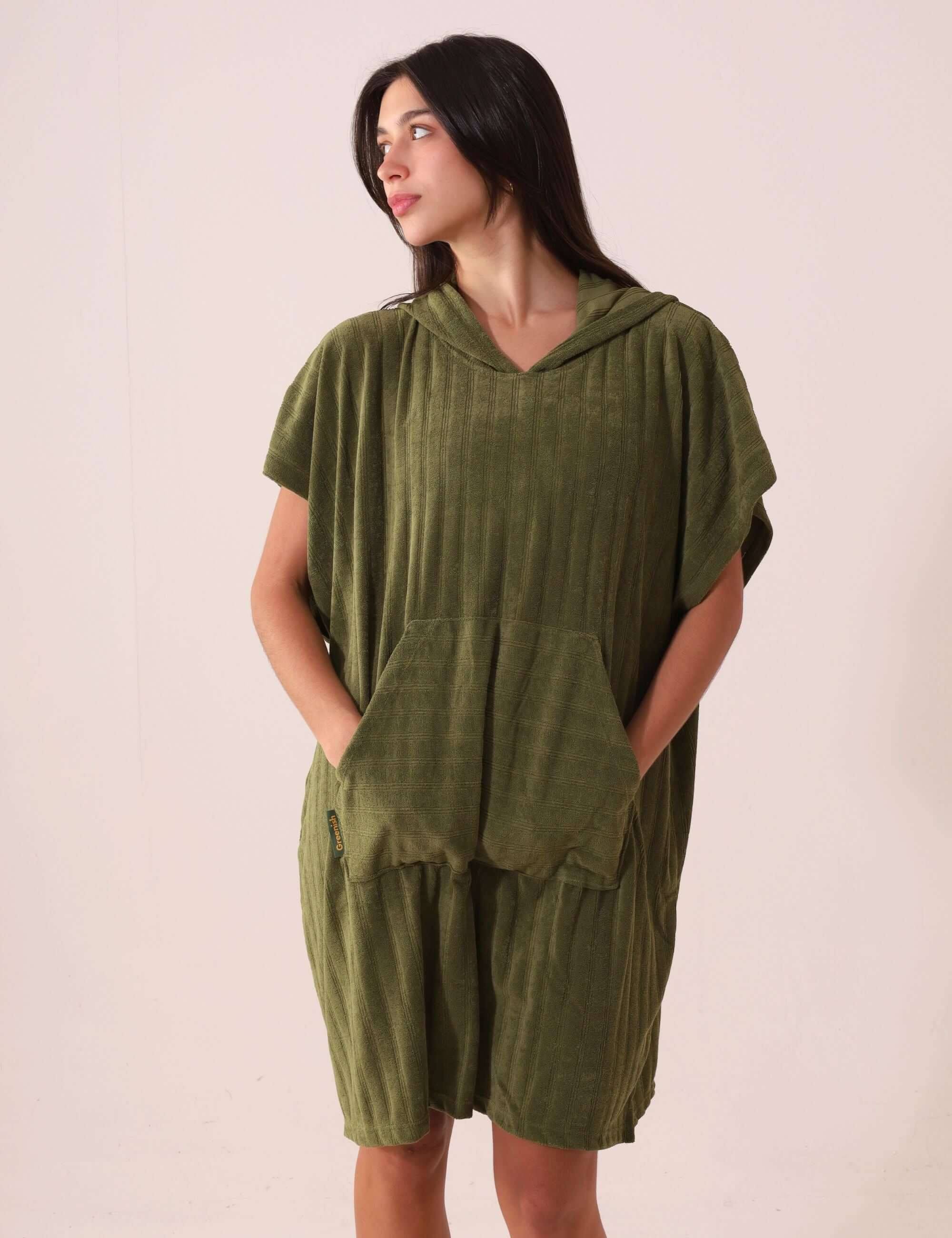 Mulher vestindo PONCHO CURTO CANELADO - VERDE da Greenish, com bolsos modelo canguru e tecido atoalhado, ideal para esportes aquáticos.