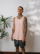 Modelo masculino usando regata rosa da marca Greenish, com tatuagens, em ambiente natural e descontraído.