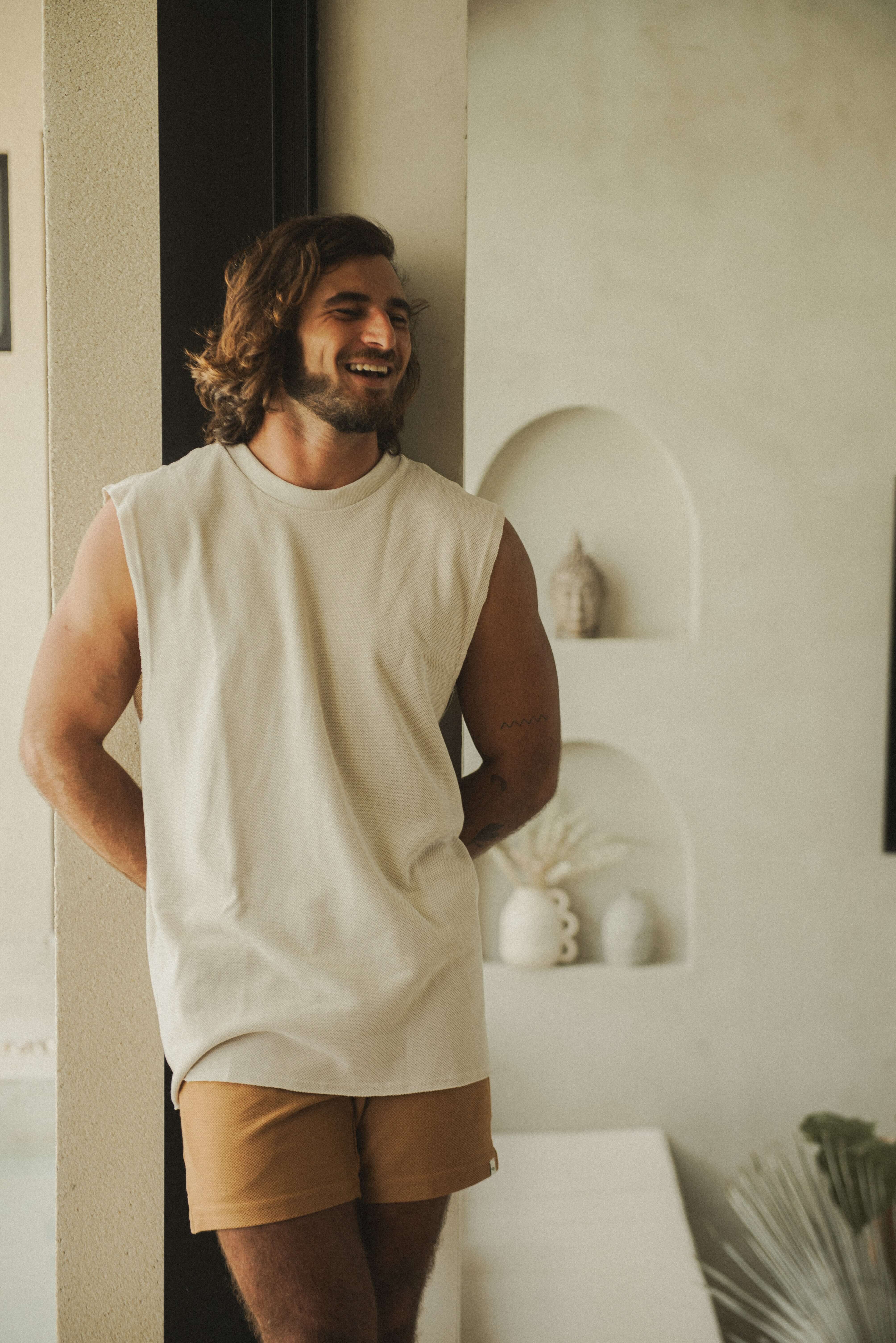 Homem usando Regata Larga Waves - Bege da marca Greenish, destacando estilo casual em ambiente interno.