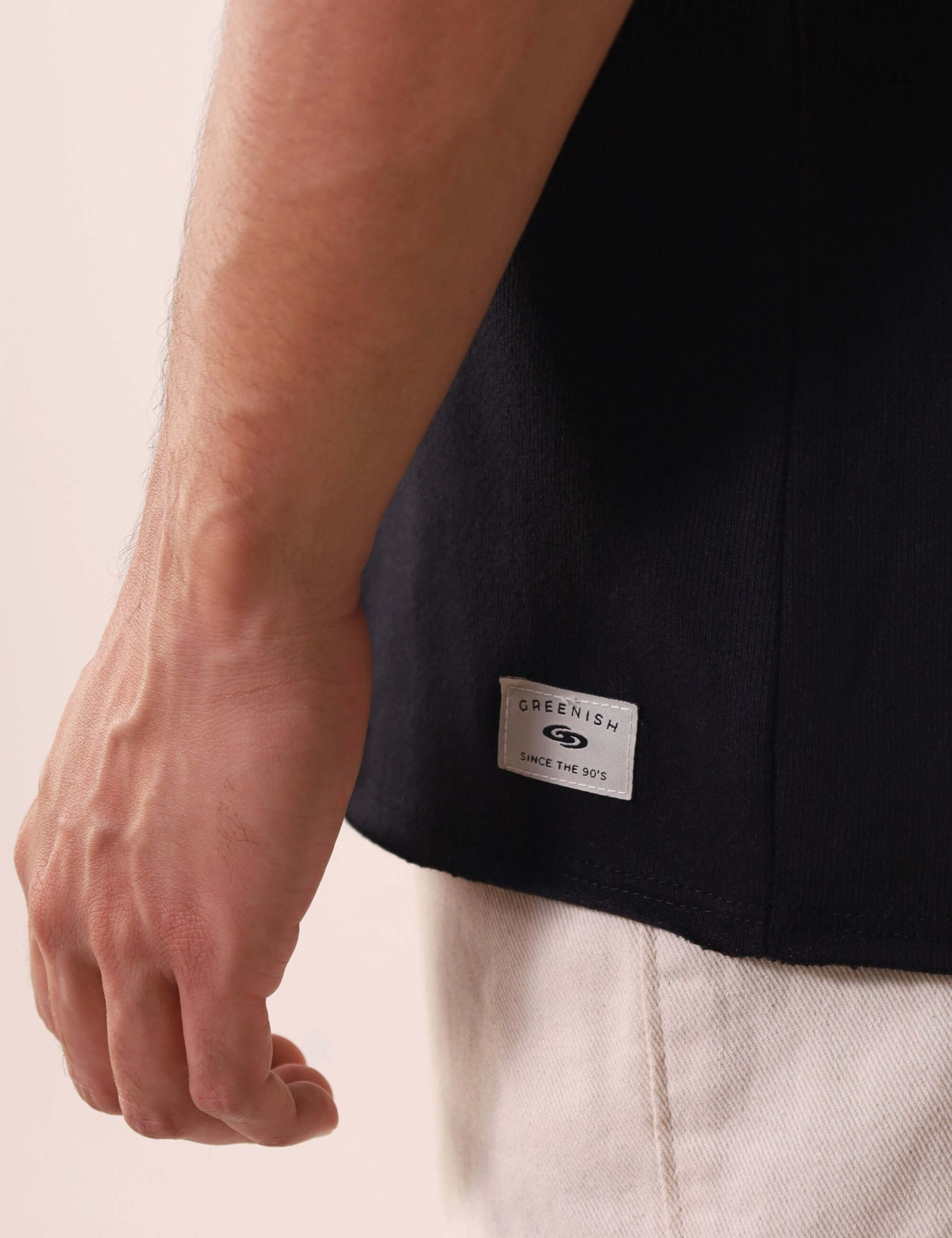 Detalhe da REGATA LARGA WAVES - PRETO da Greenish com etiqueta na base, tecido 100% algodão para conforto diário ao ar livre.