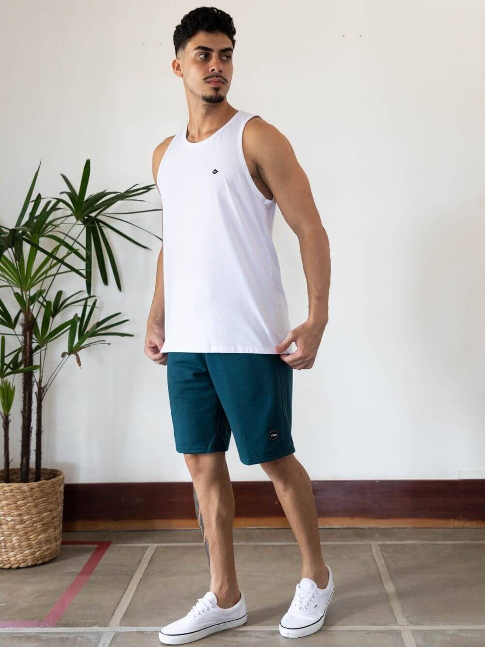 Model wearing Regata Malha Basic branca da Greenish, com calção e tênis brancos, em ambiente moderno.