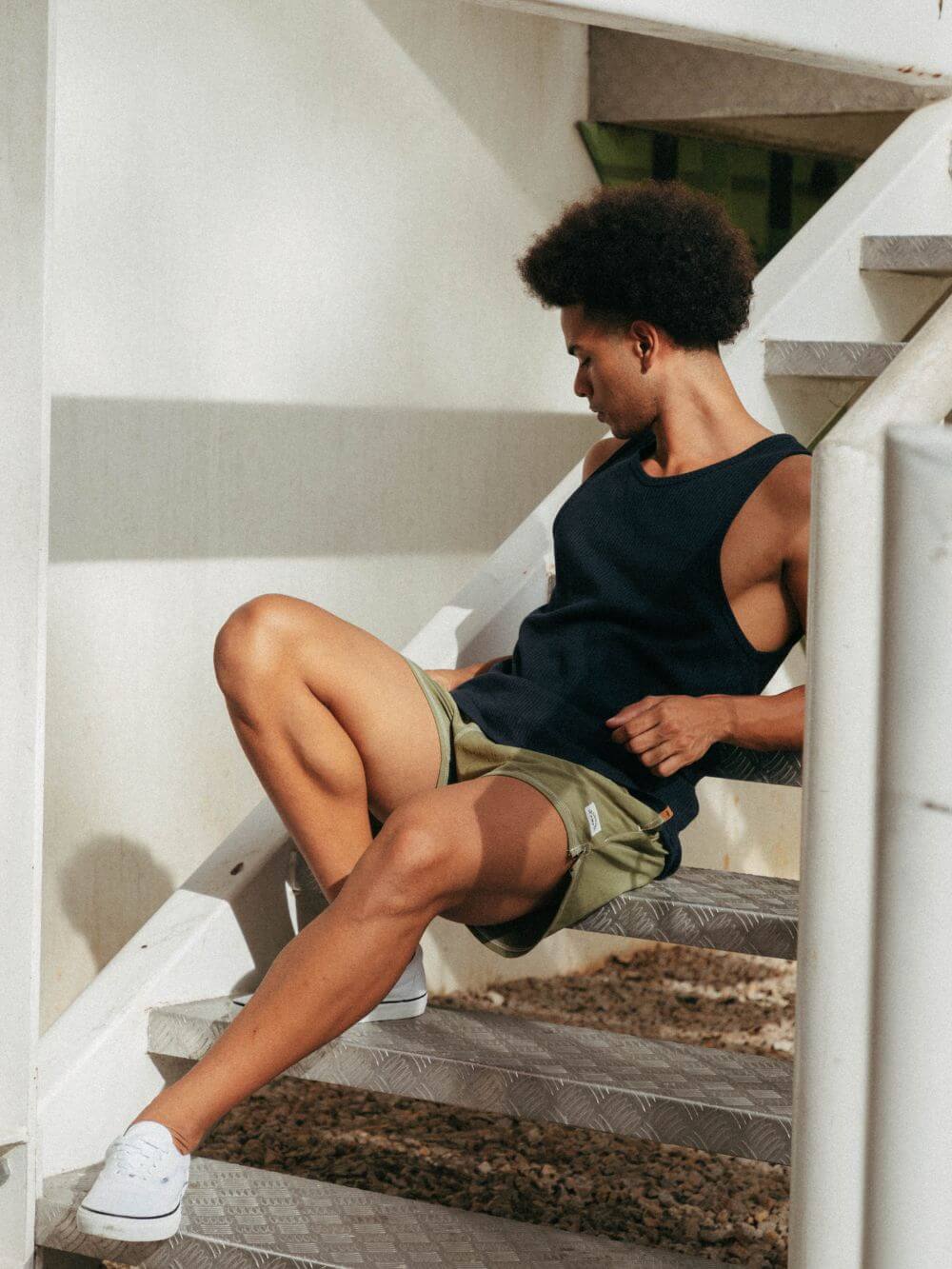 Modelo usando regata ribbed azul marinho da Greenish, sentado em escadas, estilo minimalista e confortável.