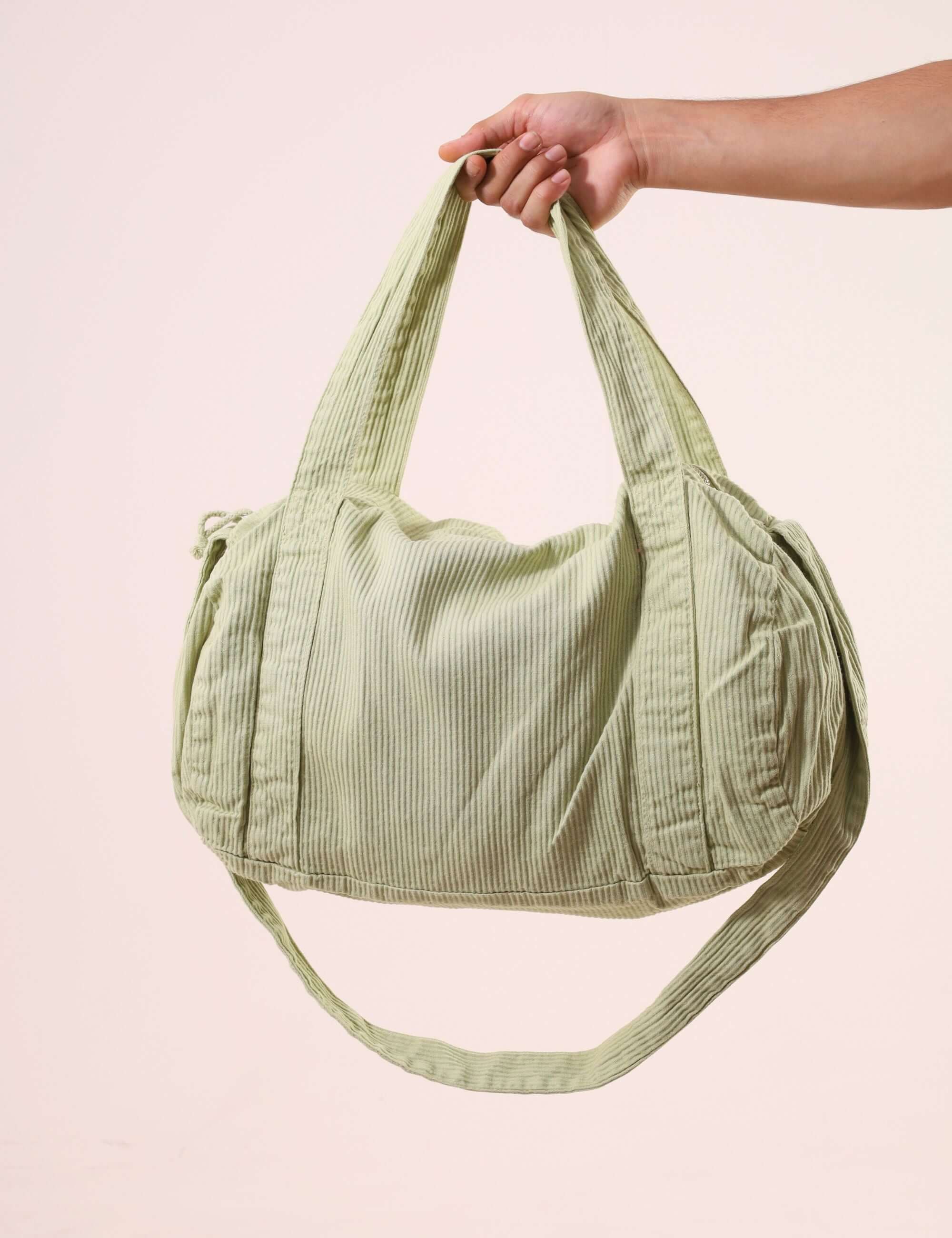 Pessoa segurando Sacola Duffel Bag - Verde Claro, feita de sarja peletizada e alças reforçadas, ideal para uso diário e estilo ao ar livre.