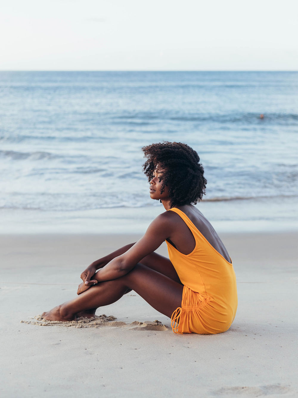 Saída de Praia Hanna laranja da marca Greenish, modelo com decote em U, sentada na areia da praia.