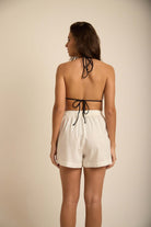 Shorts ISIS na cor off white, da marca Greenish, exibido em modelo feminino, mostrando visual traseiro.