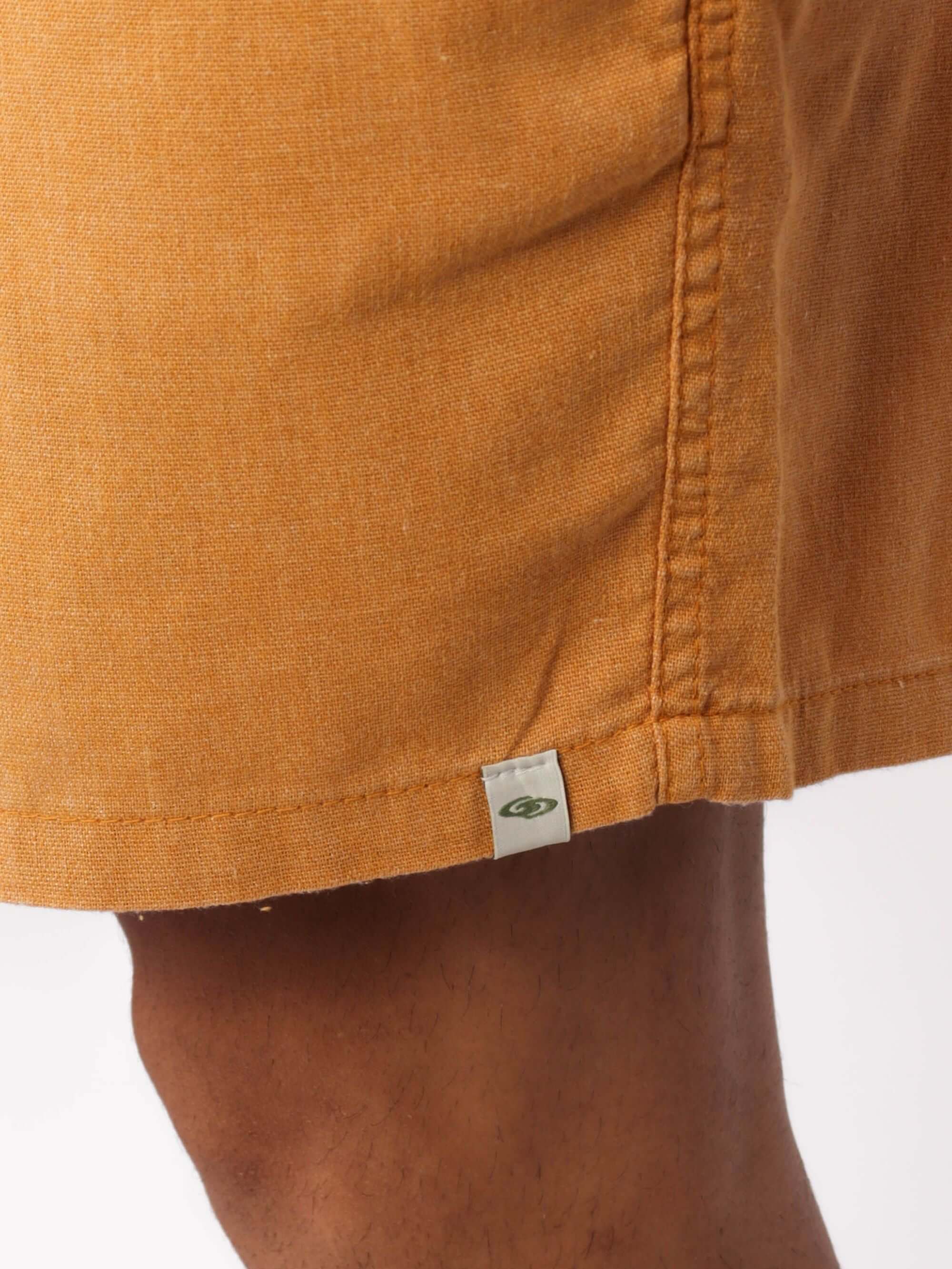 Detalhe do short de linho relax tinturado amarelo escuro da Greenish, mostrando costura e etiqueta.
