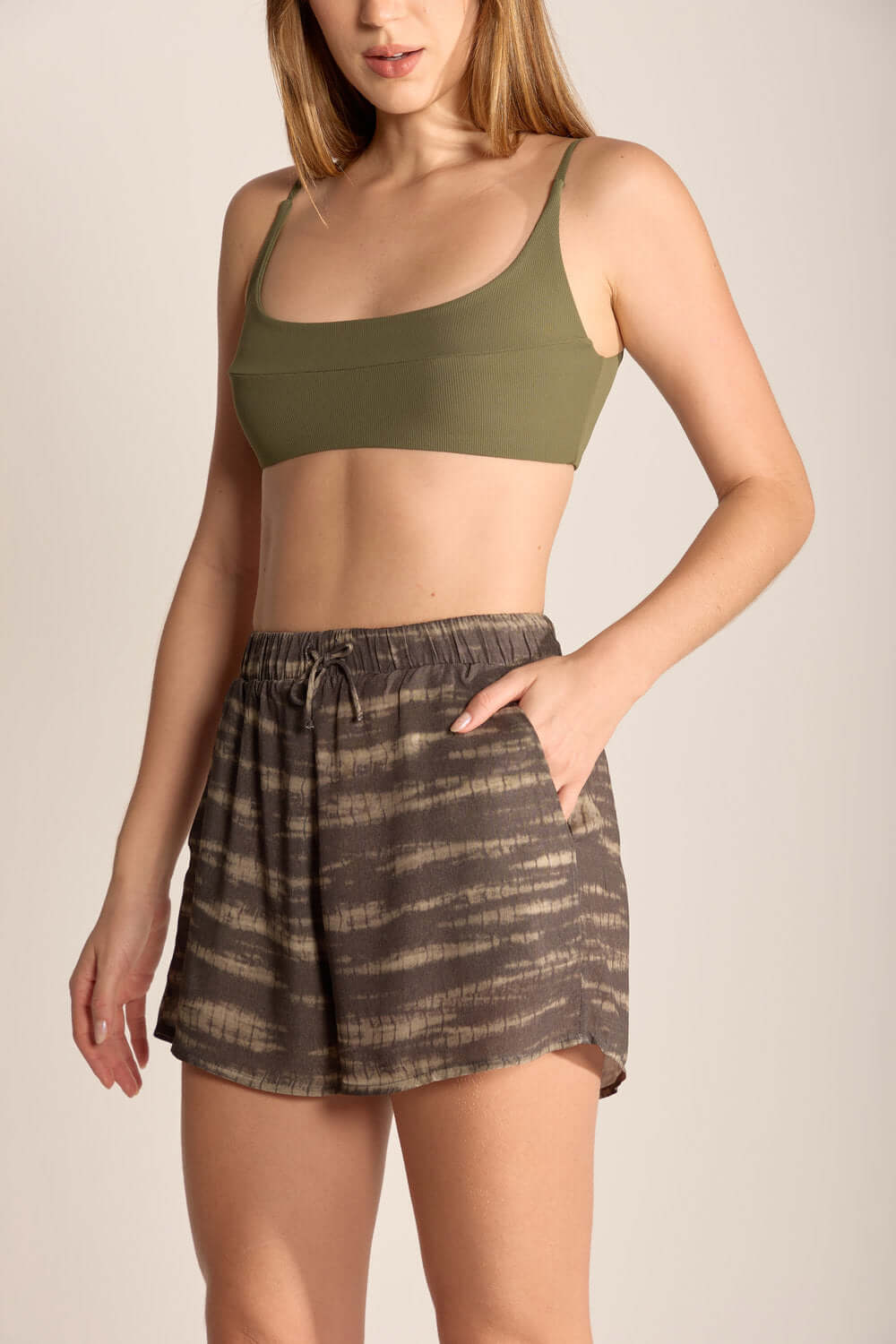Woman wearing green crop top and brown patterned shorts, showcasing casual beachwear style and comfort.