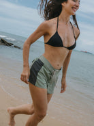 Mulher correndo na praia usando shorts esportivos verde da Greenish, confortáveis e resistentes.