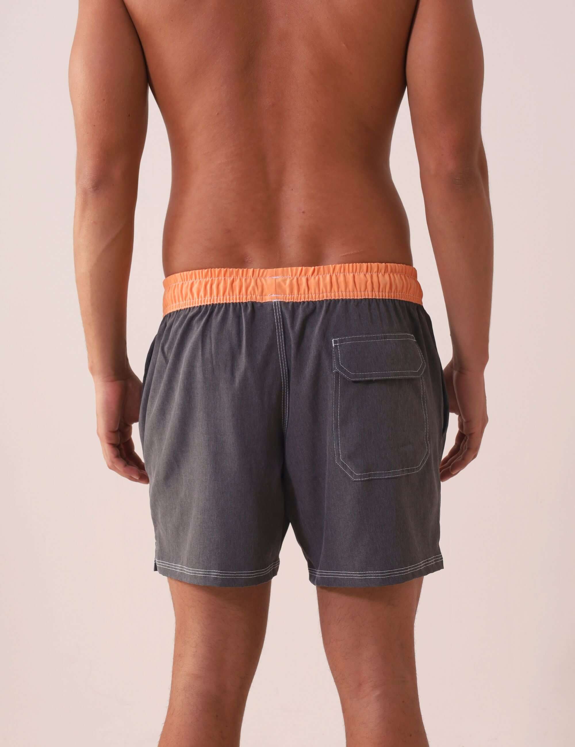 Homem usando SHORT VÔLEY BLEND - GRAFITE da Greenish com cós laranja, bolso traseiro e costura branca em contraste.