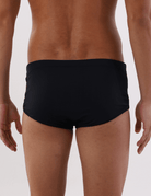 Modelo masculino vestindo sunga cavada preta básica Greenish. Vista traseira para mostrar o design confortável e ajustado.