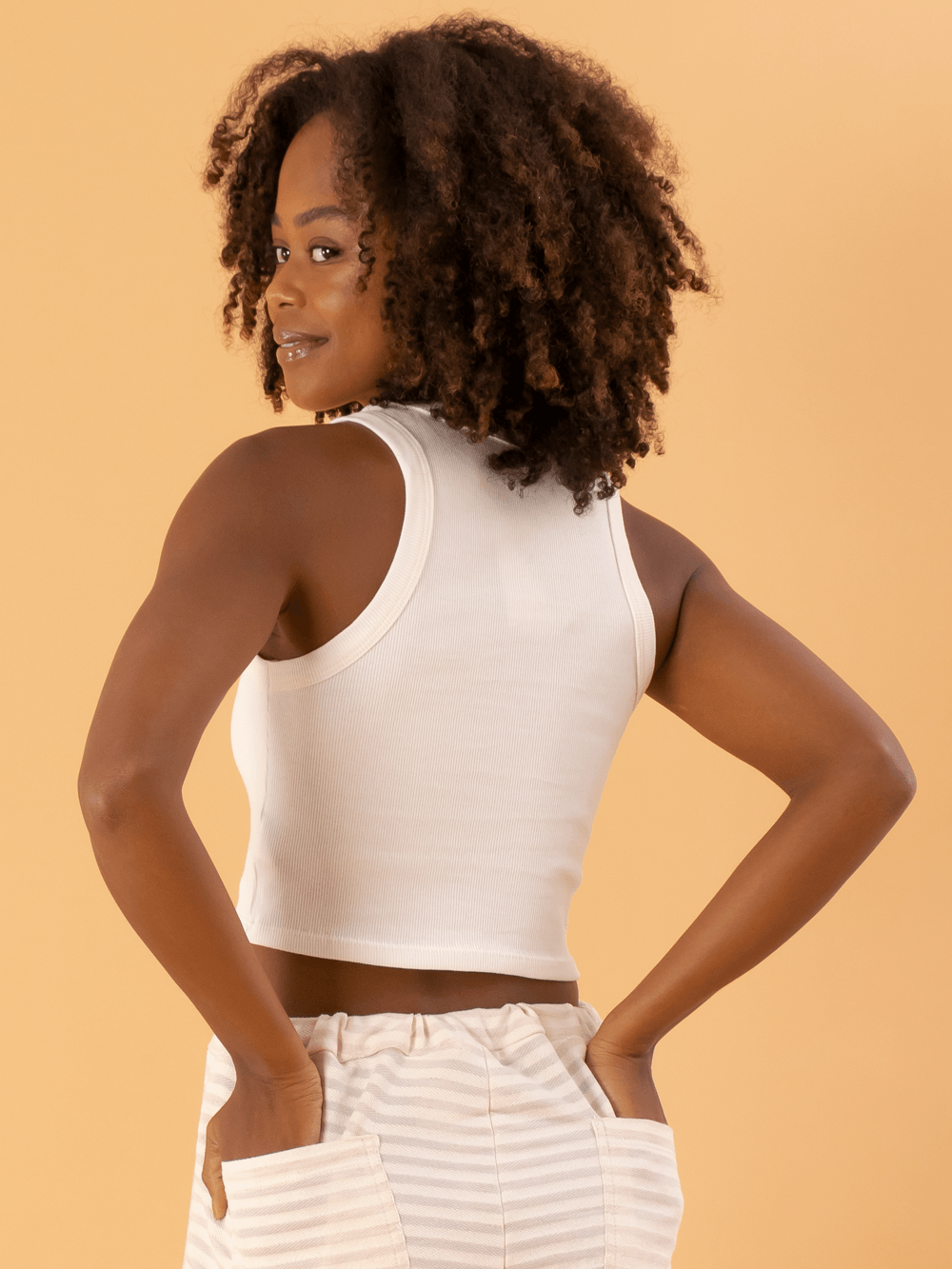 Top cropped básico em ribana off white da marca Greenish, ajustado e estiloso, exibindo costas e cabelo cacheado.