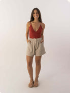 Modelo usando o Top Liz da marca Greenish, com shorts claros, sorriso alegre em fundo neutro.