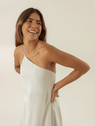 Modelo sorrindo usando vestido curto Kim off white da marca Greenish, com detalhe de alça única.
