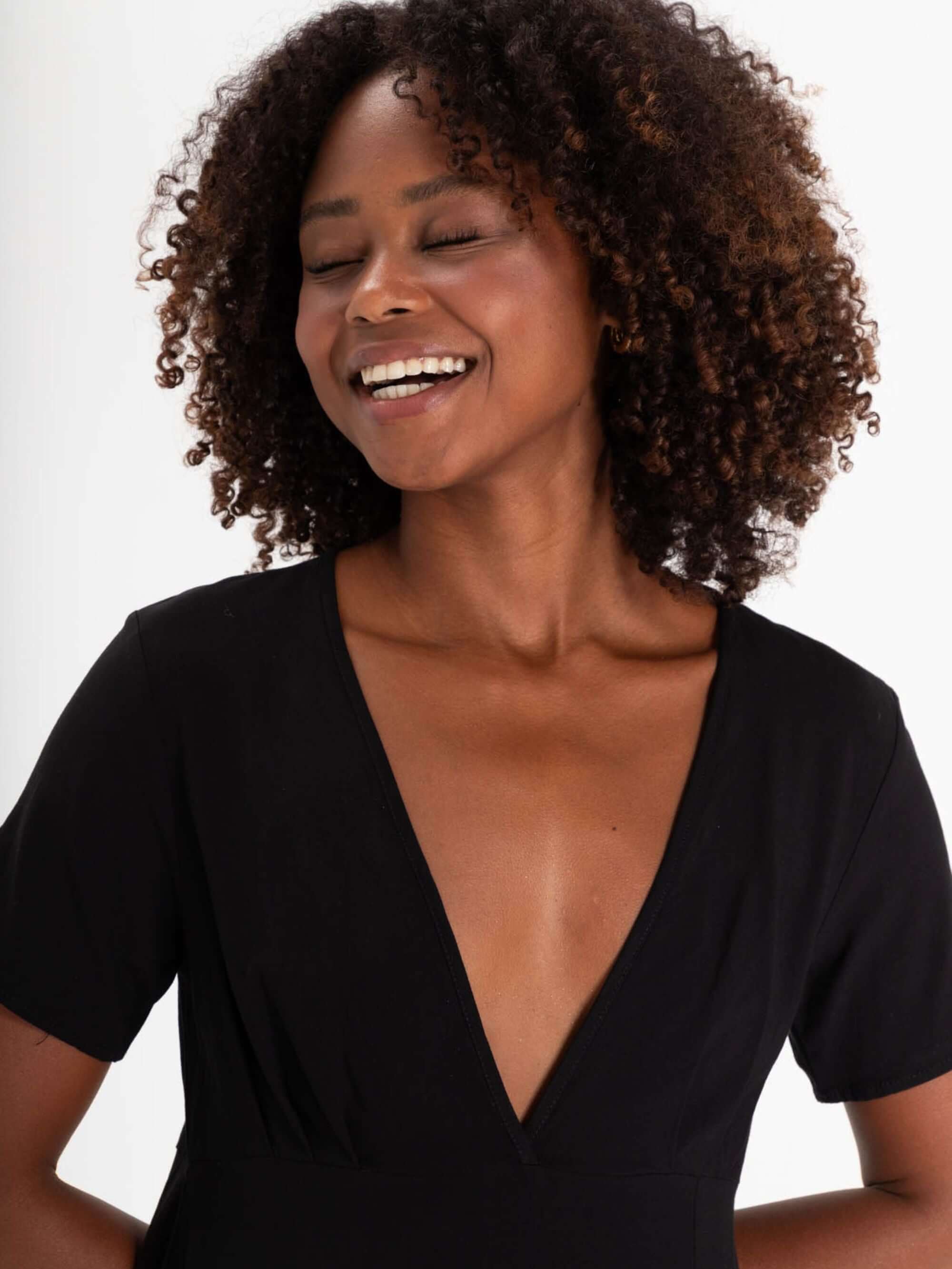 Modelo sorrindo usando o Vestido Curto Olive - Preto da marca Greenish, com decote em V e mangas soltas, ideal para o verão.
