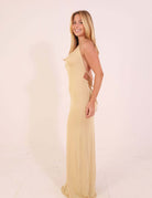 Model wearing Vesstido Longo Malha Iris - Areia in a light, airy fabric with elegant draping and side tie, perfect for warm, sunny days.