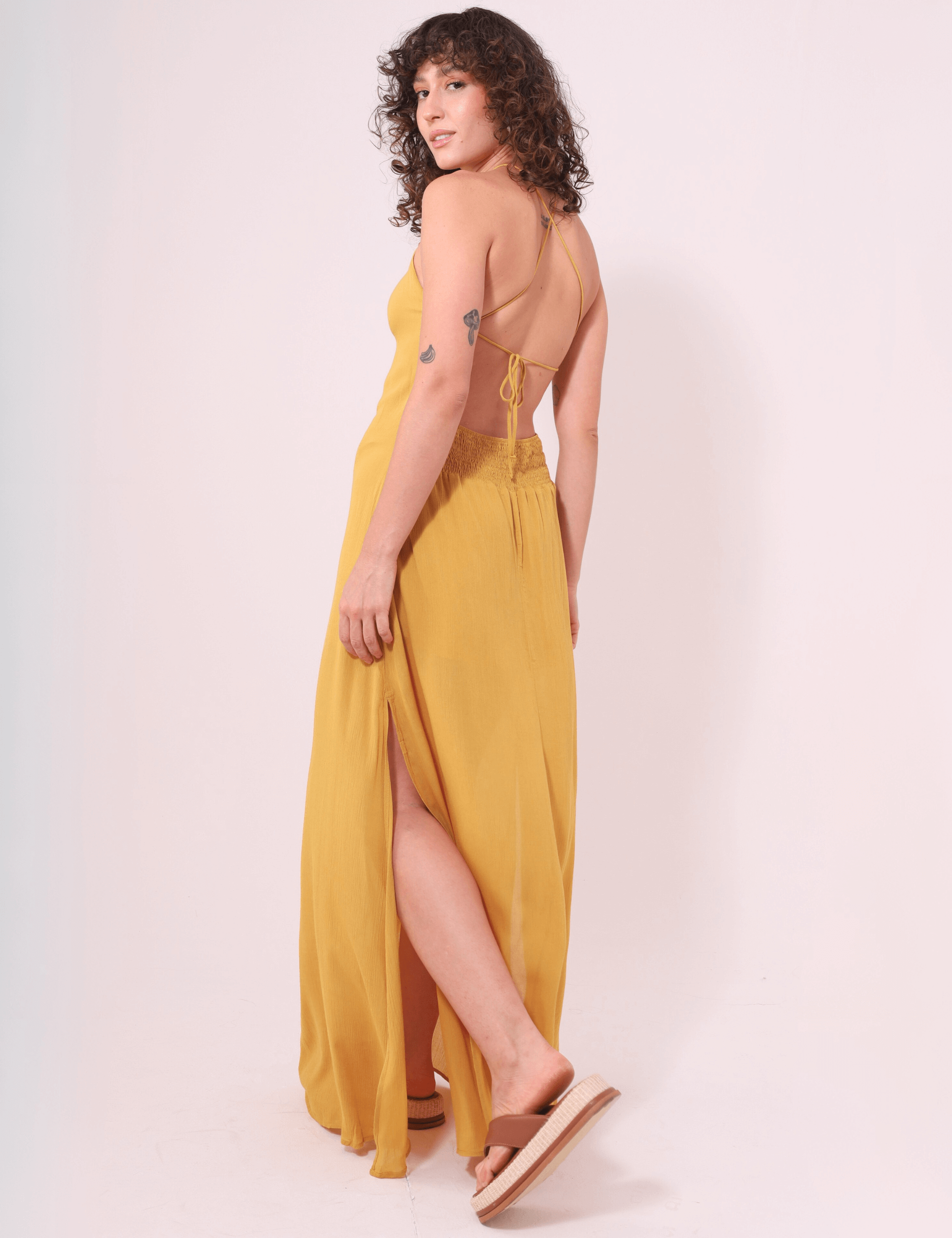 Modelo vestindo Vestido Longo Rachel Mostarda da Greenish, com alças finas, costas cruzadas e fendas laterais elegantes.