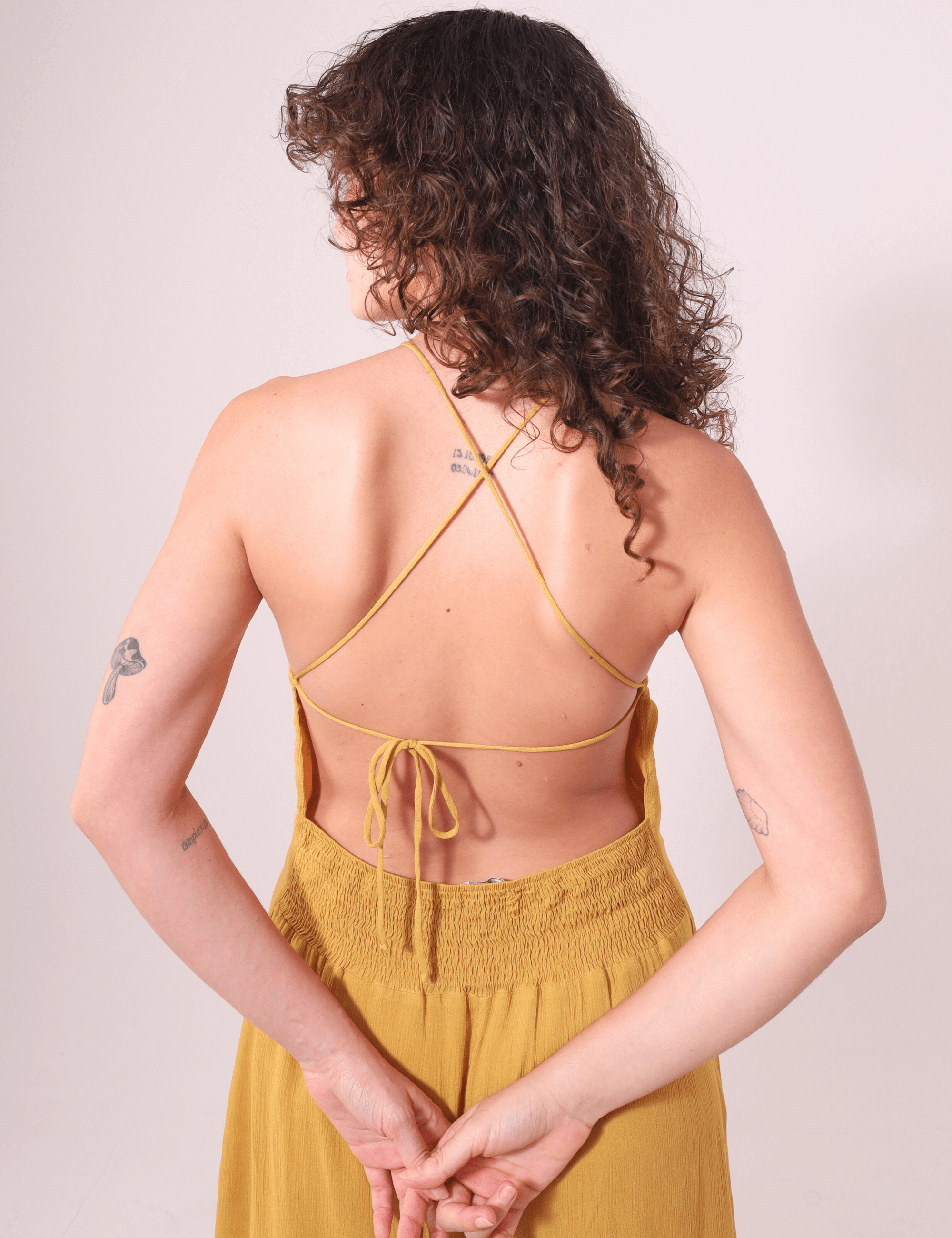 Mulher de costas vestindo Vestido Longo Rachel Mostarda, alças finas e costas cruzadas, da marca Greenish. Elegância leve e fluida.