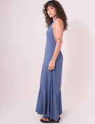 Alt Tag: Mulher vestindo Vestido Longo Serea Azul Jeans da Greenish, com decote profundo e detalhe jabô na barra para um look leve e marcante.