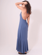 Mulher usando Vestido Longo Serena Azul Jeans Greenish com decote profundo e jabô na barra. Ideal para dias de calor.