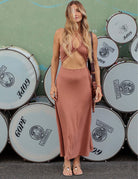 Mulher vestindo o Vestido Midi Riviera - Cacau, da marca Greenish, com busto drapeado e saia solta, em frente a tambores.