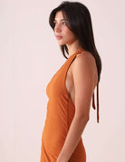 Modelo vestindo o Vestido Monique – Cacau, destacando o design de um ombro só com fita dupla para amarração em tom de marrom.